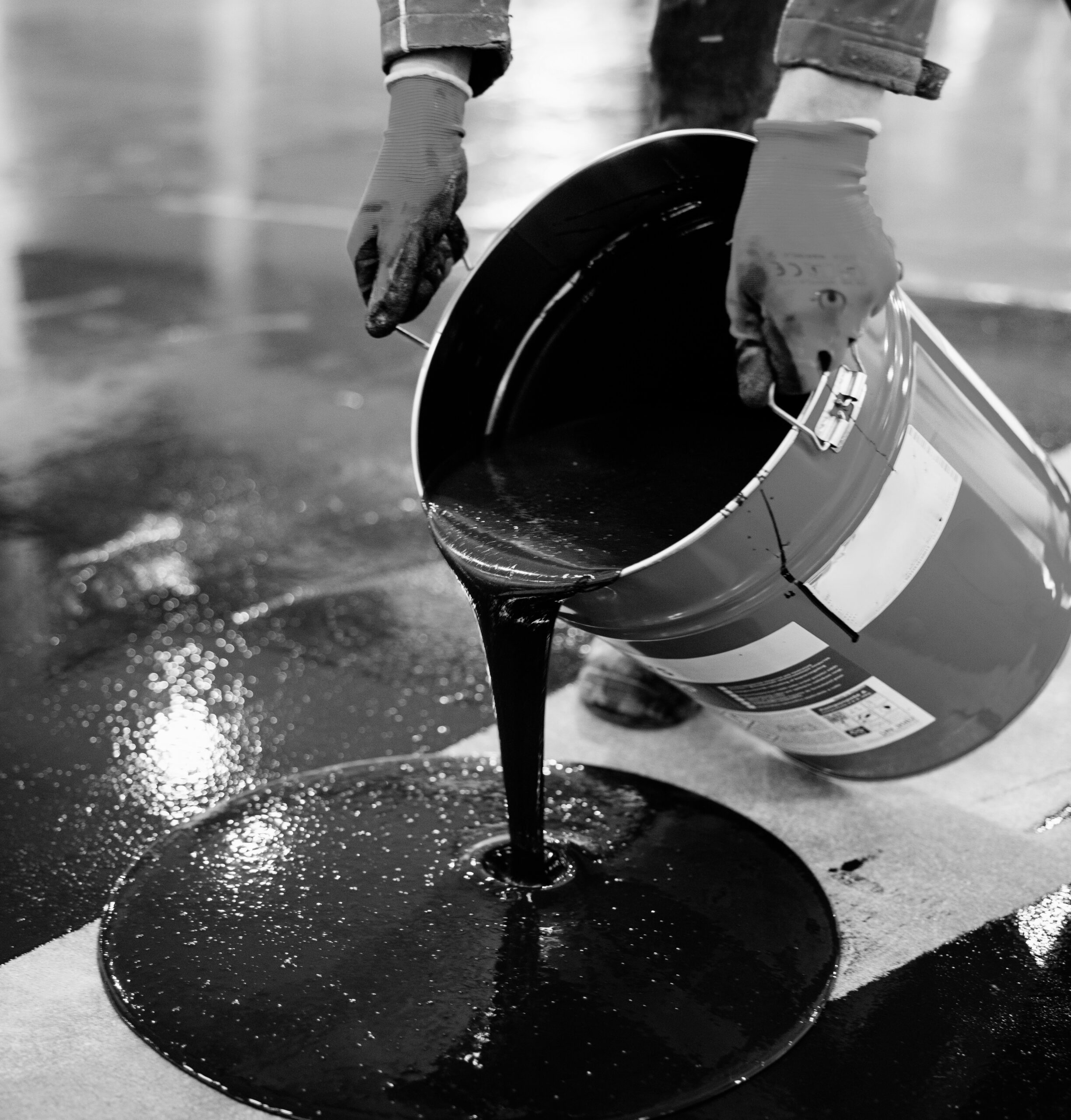 Close-up shot of a worker applying black epoxy resin from a bucket